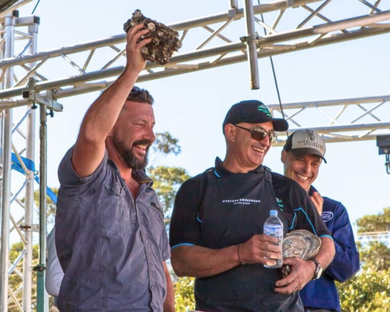 Oyster farmer Kirk Hargreaves holds his winning oyster high above his head in victory, it weighs almost 2 kilograms.