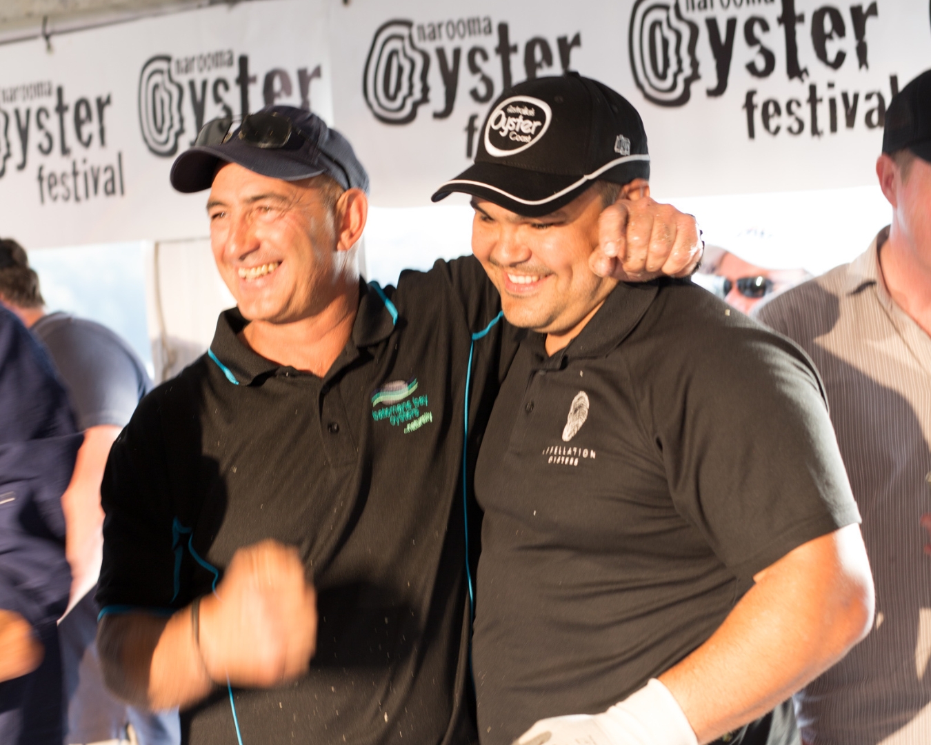 Two men are stading by a bench of shucked oysters. They are emb racing and congratulating each other on a good race.