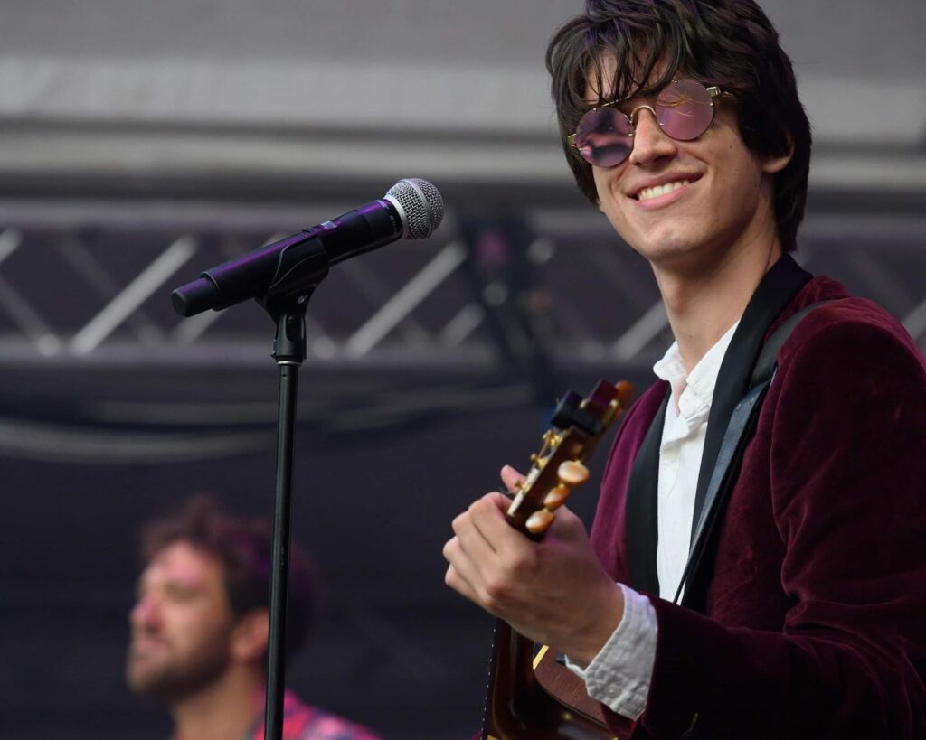 Jackson Carroll plays guitar, he's wearing sunglasses and smiling