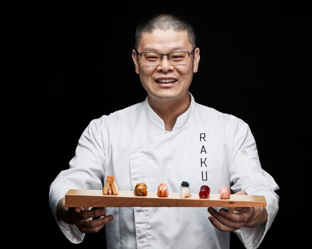 Raku founder Chef Hao Chen holds a sushi board with 6 delectable looking suhsi treats.