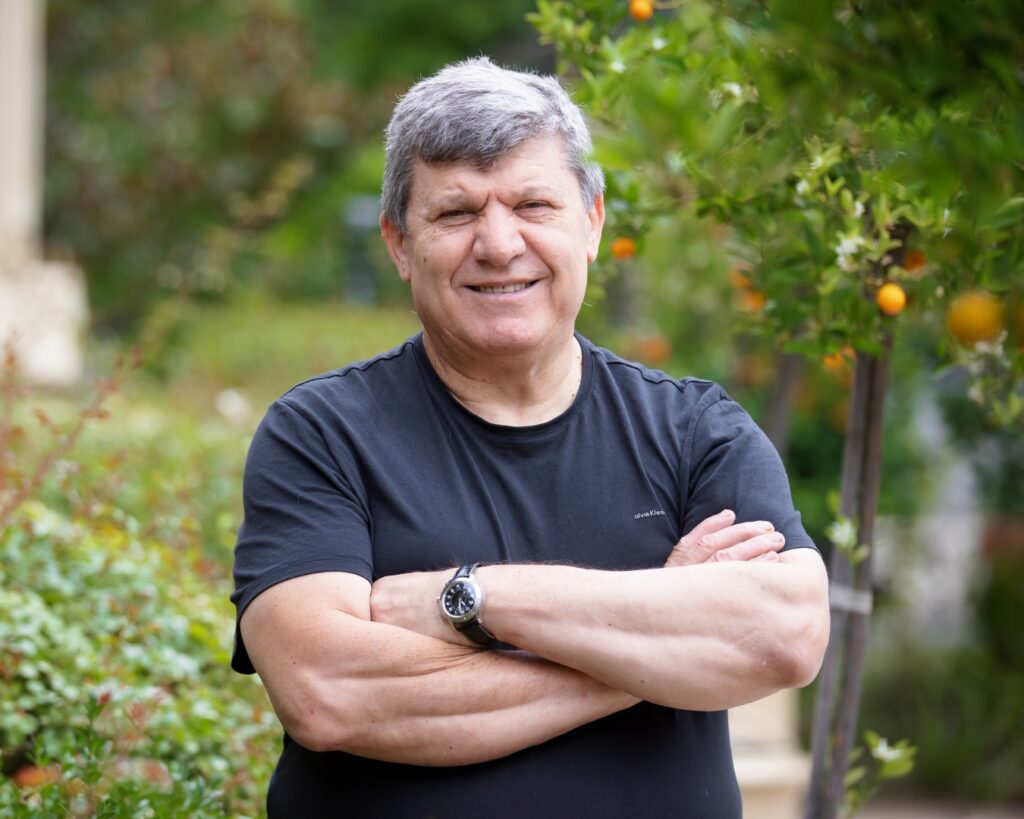 Legendary chef Serif Kaya is standing in an orchard with his arms folded, smiling at the camera.