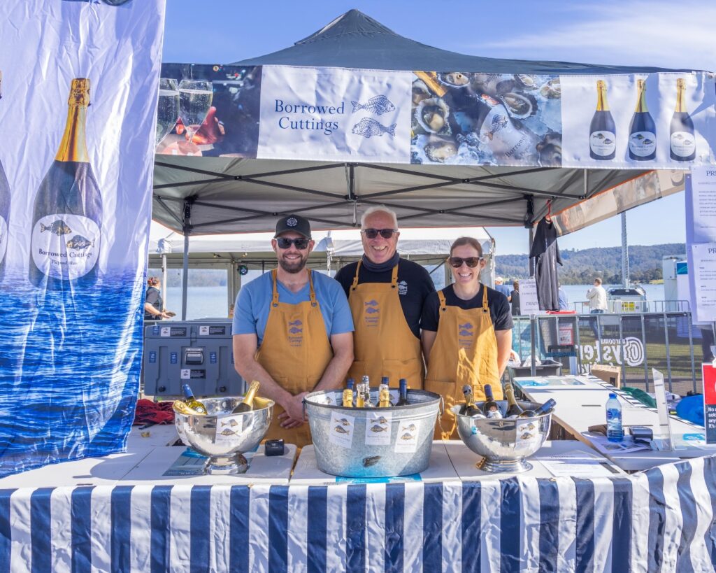 two men and a woman wearing aprons stand behind their stall, they are selling wine